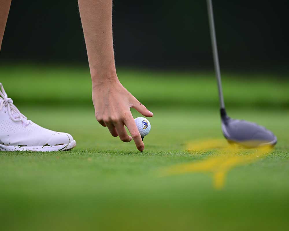 Kent State golfer placing a golf ball on a tee